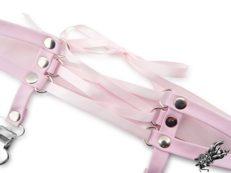 Close-up of a pink corset lacing thigh garter, showing the silver metal rivets securely attaching the pink satin ribbon ties in a criss-cross corset lacing style. The adjustable ribbon ties ensure a comfortable and versatile fit, blending style and functionality effortlessly. A perfect alternative thigh garter for brides and weddings, as well as alternative fashion styles such as pastel goth, kawaii and Japanese fashion. Displayed on a white background.