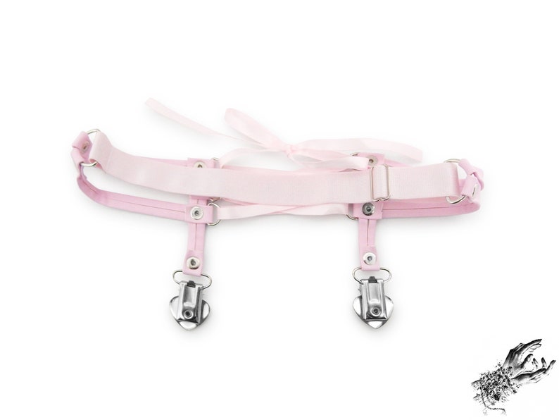 Rear view of a pink corset lacing thigh garter, showing the stretchy pink elastic strap with slider adjustment, ensuring a comfortable and versatile fit. Perfect for pastel goth, kawaii and Japanese fashion lovers, this pink thigh garter makes a bold addition to alternative fashion wardrobes. It is also an alternative option for bridal garters and alternative weddings, making a bold and unique statement on your special day. Displayed on a white background.