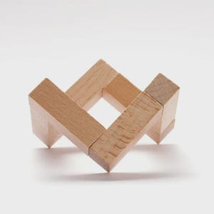 May include: A wooden puzzle with a square centre and interlocking pieces. The puzzle is made of light-coloured wood and has a geometric design. The pieces are arranged to form a three-dimensional shape.