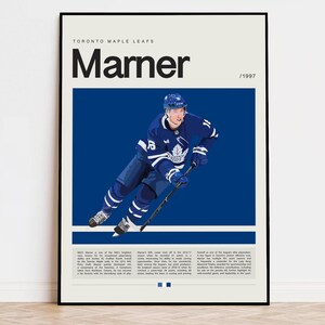 Puede incluir: Un póster de hockey de los Toronto Maple Leafs en azul y blanco con un jugador en acción. El póster tiene el texto "Marner / 1997" en la parte superior.