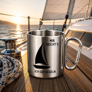 Könnte beinhalten: Ein Edelstahlbecher mit Karabinergriff, der mit einer schwarzen Grafik eines Segelboots und dem deutschen Text "MIR REICHT'S ICH GEH SEGELN" auf der Vorderseite bedruckt ist. Der Becher hat eine gebürstete Metalloberfläche.