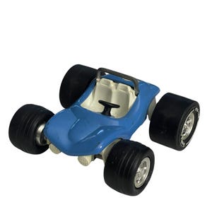 May include: A blue toy car with large black tires and a white interior. The car has a roll bar and a steering wheel. The tires have silver rims. The toy car is a miniature version of a dune buggy.