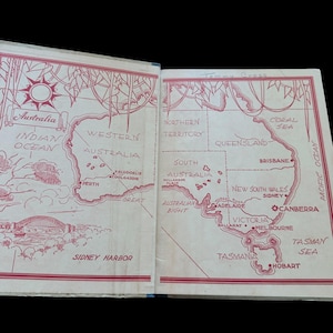 May include: An open book showing a red and white illustrated map of Australia on its endpapers. The map features labeled states, cities like Perth and Melbourne, bodies of water, and a drawing of the Sydney Harbor bridge. The text includes Australia, Indian Ocean, Pacific Ocean, and various geographic locations.