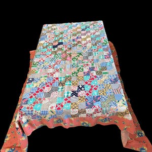 May include: A rectangular patchwork quilt featuring a grid of small, multi-colored fabric squares in various patterns including stripes, checks, and florals. The quilt is bordered by a solid coral-colored fabric with a blue and yellow floral print.