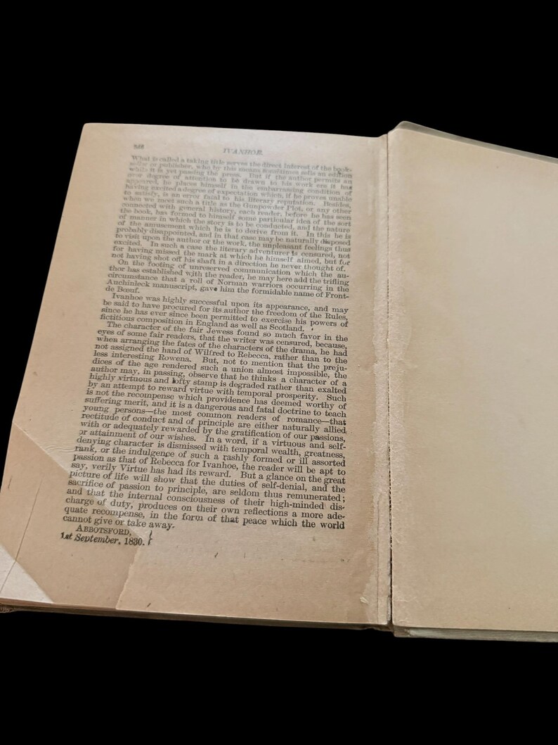 May include: An open antique book page with aged, off-white paper and black printed text. The header reads IVANHOE. The text discusses literary themes and character fates. The bottom left corner shows the text ABBOTSFORD, 1st September, 1830.