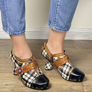 May include: A pair of unique shoes with a black and white plaid pattern, black toe caps, and brown leather straps. The heels are a distinctive curved design, and a flower adorns one shoe. The shoes are worn with blue jeans.