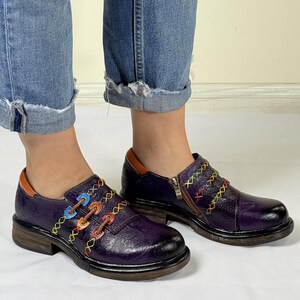 May include: Purple leather shoes with colorful stitching and a zipper detail. The shoes have a chunky heel and a rounded toe.