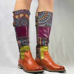 May include: A pair of brown leather knee-high boots with colorful patterned fabric accents. The boots have a zipper on the inside of each boot and a buckle on the outside.