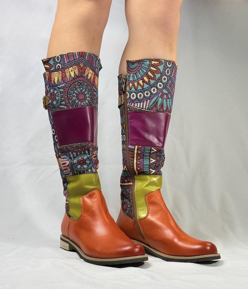 May include: A pair of brown leather knee-high boots with colorful patterned fabric accents. The boots have a zipper on the inside of each boot and a buckle on the outside.
