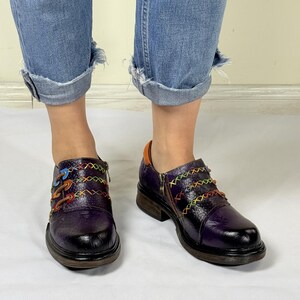 May include: Purple leather shoes with colorful stitching and a zipper detail. The shoes have a chunky heel and a rounded toe.