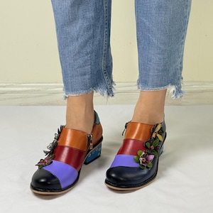 Puede incluir: Botas de tobillo de cuero multicolores con tac&oacute;n de bloque y adornos florales. Las botas tienen una combinaci&oacute;n de colores azul, morado, rojo, naranja y negro.