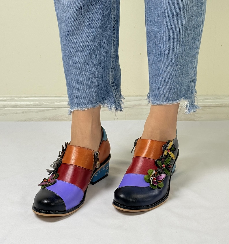 Puede incluir: Botas de tobillo de cuero multicolores con tac&oacute;n de bloque y adornos florales. Las botas tienen una combinaci&oacute;n de colores azul, morado, rojo, naranja y negro.