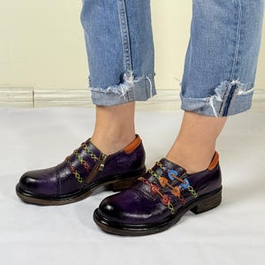 May include: Purple leather shoes with colorful stitching and laces. The shoes have a zipper on the side and a chunky heel.