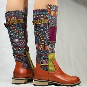 May include: A pair of brown leather knee-high boots with a colorful patterned fabric upper. The boots have a buckle strap and a zipper on the inside of the boot.