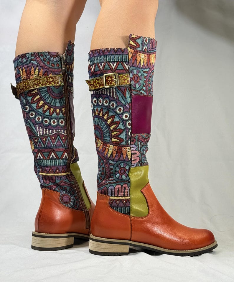 May include: A pair of brown leather knee-high boots with a colorful patterned fabric upper. The boots have a buckle strap and a zipper on the inside of the boot.