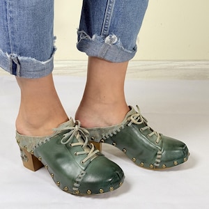 May include: Green leather clogs with a lace-up front and a wooden heel. The clogs have a distressed look and are decorated with metal studs.