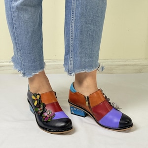 Puede incluir: Botas de tobillo de cuero multicolores con tac&oacute;n de bloque y adornos florales decorativos. Las botas tienen una cremallera lateral y una combinaci&oacute;n de colores azul, rojo, naranja y morado.