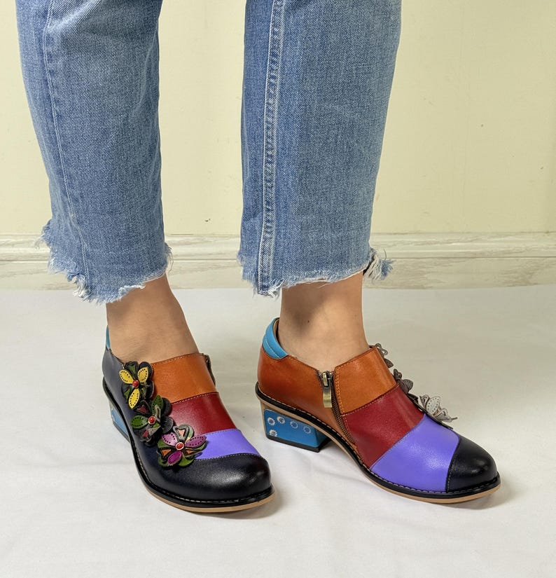 Puede incluir: Botas de tobillo de cuero multicolores con tac&oacute;n de bloque y adornos florales decorativos. Las botas tienen una cremallera lateral y una combinaci&oacute;n de colores azul, rojo, naranja y morado.