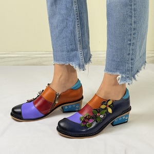 Puede incluir: Zapatos de cuero multicolores con un esquema de colores azul, morado, rojo y naranja. Los zapatos tienen un peque&ntilde;o adorno floral en la punta y una cremallera en el lateral. Los zapatos tienen un tac&oacute;n de bloque.