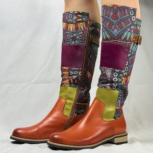 May include: A pair of knee-high boots with a brown leather upper and a patterned fabric shaft. The fabric is a mix of blue, green, purple, and orange colors with geometric designs. The boots have a zipper on the inside of the shaft and a buckle on the outside.