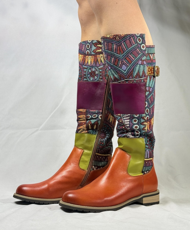 May include: A pair of brown leather knee-high boots with a colorful patterned fabric upper. The boots have a zipper on the inside of each boot and a buckle on the outside of each boot.