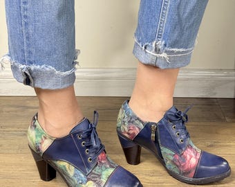 May include: Blue leather lace-up shoes with floral print accents. The shoes have a rounded toe, a side zipper, and a stacked heel. The floral pattern includes pink, green, and yellow hues.