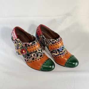 May include: A pair of colorful ankle boots with a floral and leopard print design. The boots have a green toe cap, orange leather accents, and a red flower embellishment.