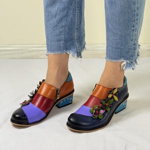 Puede incluir: Zapatos de tac&oacute;n de cuero multicolores con adornos florales. Los zapatos tienen una combinaci&oacute;n de colores azul, morado, rojo y naranja. Los tacones son de color azul claro con lunares blancos.