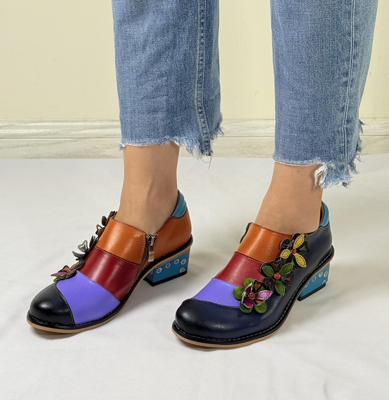 Puede incluir: Zapatos de tac&oacute;n de cuero multicolores con adornos florales. Los zapatos tienen una combinaci&oacute;n de colores azul, morado, rojo y naranja. Los tacones son de color azul claro con lunares blancos.
