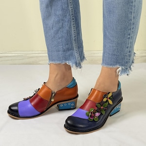 Puede incluir: Un par de zapatos de cuero coloridos con tac&oacute;n de bloque. Los zapatos tienen un dise&ntilde;o de patchwork multicolor con cuero azul, rojo, naranja y morado. Un zapato tiene un adorno floral en la punta.