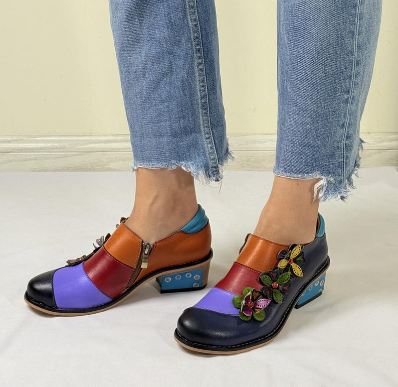 Puede incluir: Un par de zapatos de cuero coloridos con tac&oacute;n de bloque. Los zapatos tienen un dise&ntilde;o de patchwork multicolor con cuero azul, rojo, naranja y morado. Un zapato tiene un adorno floral en la punta.