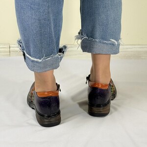 May include: A pair of purple leather shoes with orange and green accents. The shoes have a woven design and a zipper on the side.
