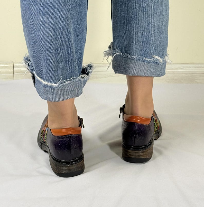May include: A pair of purple leather shoes with orange and green accents. The shoes have a woven design and a zipper on the side.