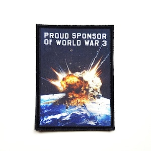 Op de afbeelding: Een rechthoekige patch met de tekst "PROUD SPONSOR OF WORLD WAR 3" boven een illustratie van een explosie boven de aarde. De patch heeft een zwarte rand en een donkerblauwe achtergrond.