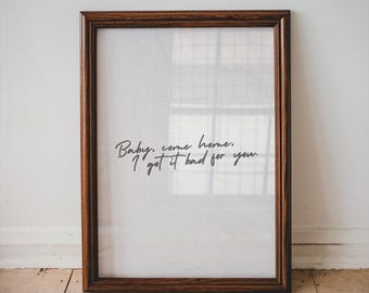 May include: A framed print with a dark brown wooden frame. The print features the handwritten text "Baby, come home. I got it bad for you" in black script on a white background. The frame is rectangular.