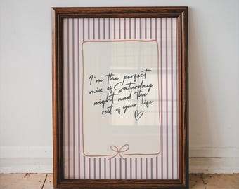 May include: A framed print with a dark brown wooden frame. The print features a cream-colored rectangle with the handwritten text, "I'm the perfect mix of Saturday night and the rest of your life" and a small heart. The background has vertical purple and white stripes.