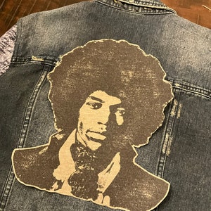 May include: A denim jacket with a vintage-style patch of a man with an afro. The patch is brown and black and features a close-up of the man's face.