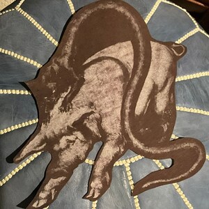 May include: A brown cat-shaped decorative item with a textured surface. The cat's tail arches over its back, and a smaller cat is perched on its back. The item is cut out and appears to be made of paper or cardboard.