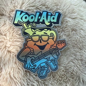 May include: A colorful Kool-Aid patch featuring a cartoon pitcher character playing a guitar. The pitcher is wearing sunglasses and a bandana. The text "Kool-Aid" is in rainbow colors.