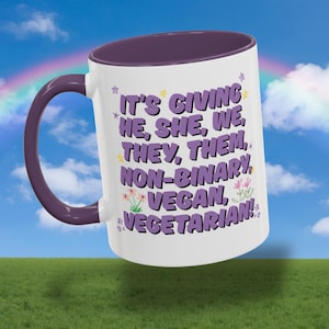 Puede incluir: Taza de cerámica blanca con interior y asa morados. La taza presenta el texto "IT'S GIVING HE, SHE, WE, THEY, THEM, NON-BINARY, VEGAN, VEGETARIAN!" en morado, con detalles florales y estrellas. El fondo muestra un arcoíris y hierba verde.