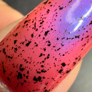 May include: Close-up of a pink nail polish with black glitter. The polish has a gradient effect, fading from pink to purple.
