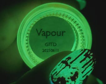 May include: A glowing green nail polish jar with the word "Vapour" printed on the label. The image also shows a painted fingernail with a matching green glow and black drip design.