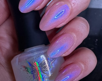 May include: A hand with long, almond-shaped nails painted with a pearlescent, iridescent polish. The nails shift in color from pink to blue, with a bright blue streak down the center. A bottle of nail polish is held in the hand.