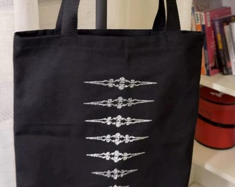 May include: Black tote bag with decorative silver embroidery. The bag features a series of horizontal embroidered designs. The tote bag has black handles and is likely made of a durable fabric, suitable for carrying various items.