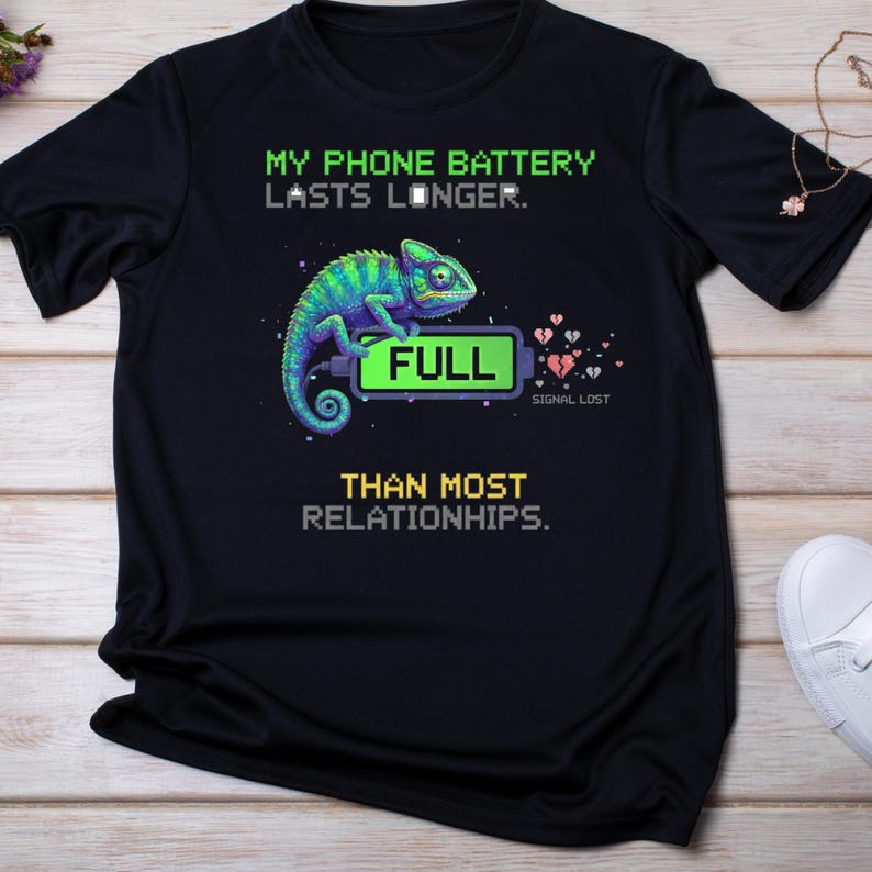 May include: Black t-shirt with a graphic of a chameleon and a battery that reads "FULL." The text above the chameleon reads "MY PHONE BATTERY LASTS LONGER." Below the chameleon, the text reads "THAN MOST RELATIONSHIPS."