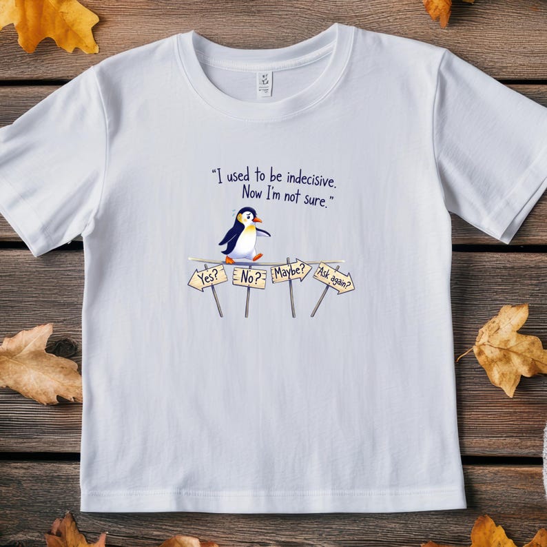 May include: White t-shirt featuring a cartoon penguin and the text "I used to be indecisive. Now I'm not sure." The penguin stands near signs that say "Yes?", "No?", "Maybe?", and "Ask again?"