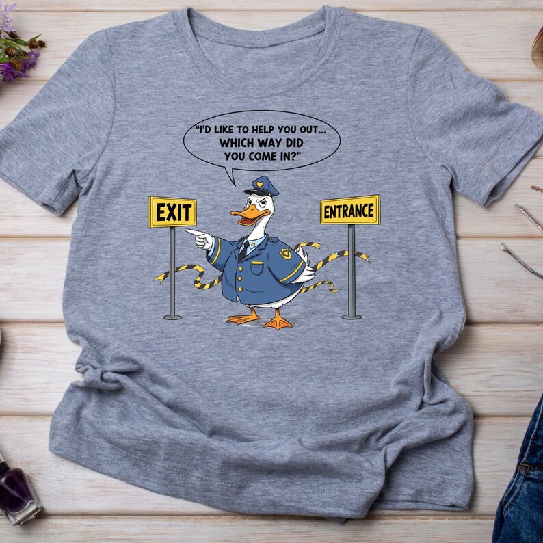 May include: A light gray t-shirt featuring a cartoon duck dressed as a police officer. The duck points towards an "EXIT" sign and has a speech bubble with the text "I'D LIKE TO HELP YOU OUT... WHICH WAY DID YOU COME IN?" and an "ENTRANCE" sign.