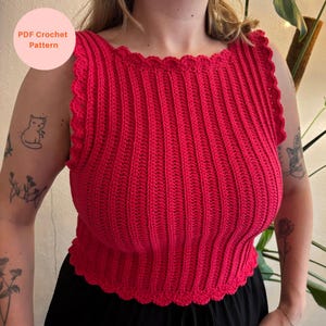 May include: A bright red sleeveless crochet top featuring a vertical ribbed texture and a scalloped edge along the neckline, armholes, and hem. A circular pink graphic in the upper left corner contains the text PDF Crochet Pattern.