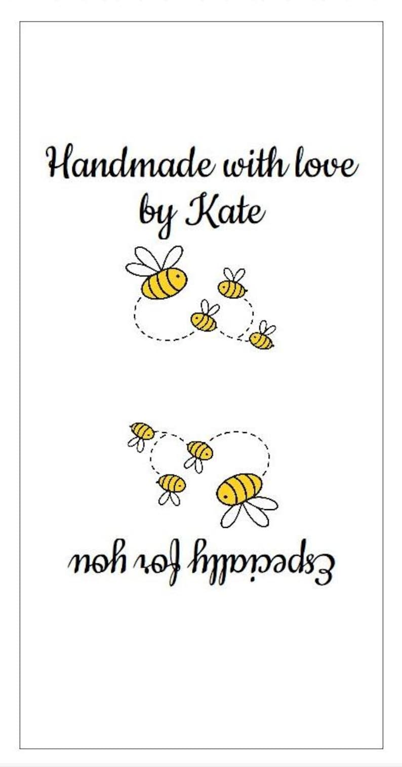 Op de afbeelding: Een rechthoekig wit label met de zwarte tekst Handmade with love by Kate bovenaan en Especially for you onderaan. Tussen de tekst staan twee groepen kleine gele en zwarte bijen met gestippelde vliegroutes.