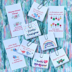 May include: A selection of white tags featuring text and illustrations, such as "Dreamy Dresses Vintage" and "Betty's Boutique." The tags are secured with silver paper clips. The background has a colourful, abstract design with shades of blue, green, and pink.